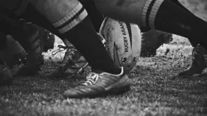Gros plan dynamique sur un ballon de rugby au cœur d'une mêlée intense.