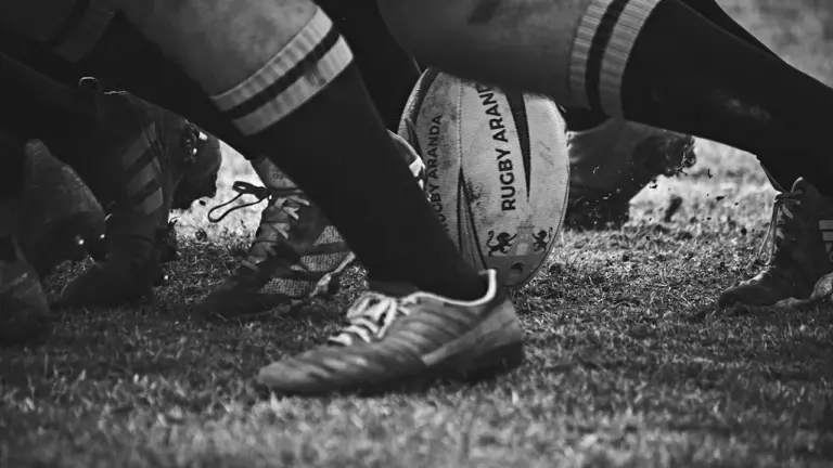 Gros plan dynamique sur un ballon de rugby au cœur d'une mêlée intense.