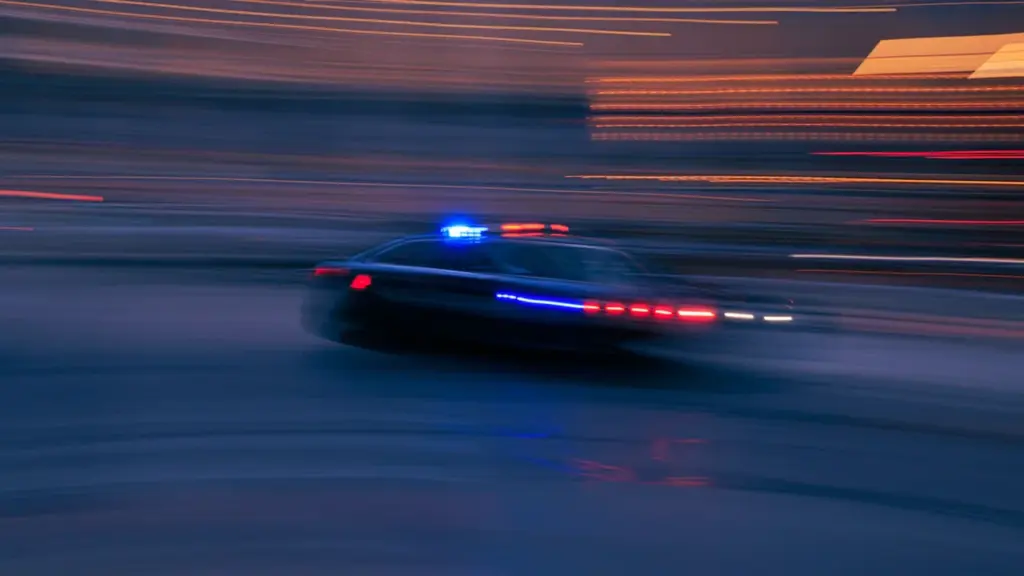 Voiture de patrouille circulant rapidement dans une rue urbaine de nuit.