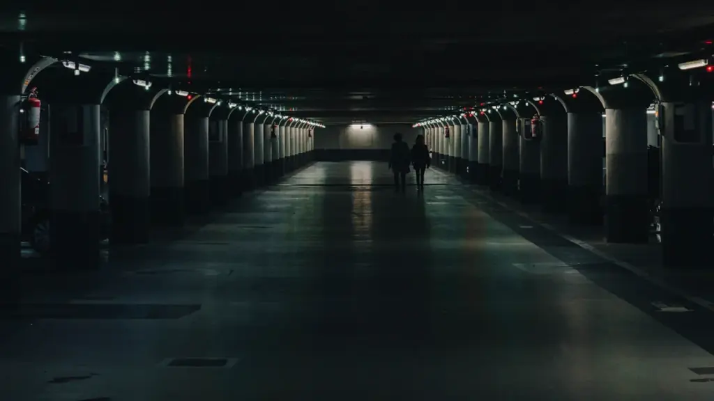 Silhouette de personnes marchant dans un parking souterrain sombre et structuré à Metz.