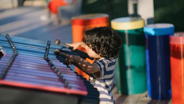 Un jeune garçon joue joyeusement d'un xylophone coloré dans un espace extérieur ensoleillé.