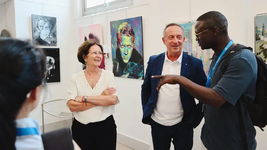 Trois personnes discutent joyeusement dans une galerie d'art entourée de peintures colorées au mur.