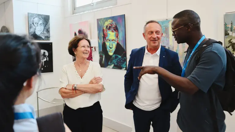 Trois personnes discutent joyeusement dans une galerie d'art entourée de peintures colorées au mur.