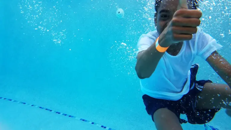Un jeune garçon sous l'eau fait un signe de pouce levé dans la piscine.