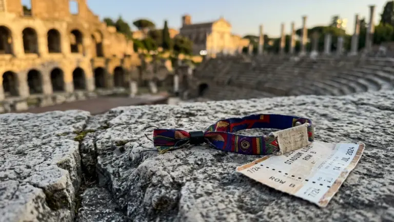 Un bracelet de festival coloré et un billet de concert posés sur une pierre antique.