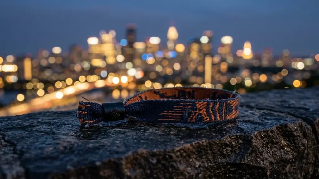 Un bracelet en tissu bleu et orange posé sur un muret face à une ville illuminée.