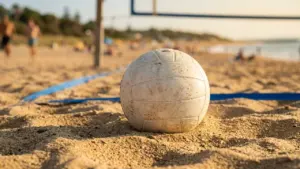 Un ballon de volley-ball blanc et sablonneux posé sur le sable d'une plage ensoleillée.