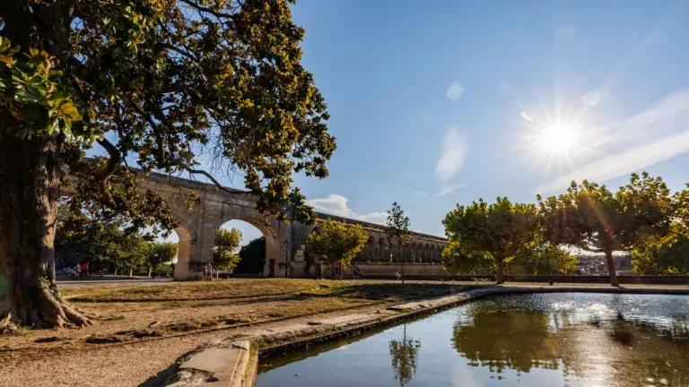 Ancien aqueduc en pierre dominant un parc ensoleillé avec un petit bassin d'eau calme.