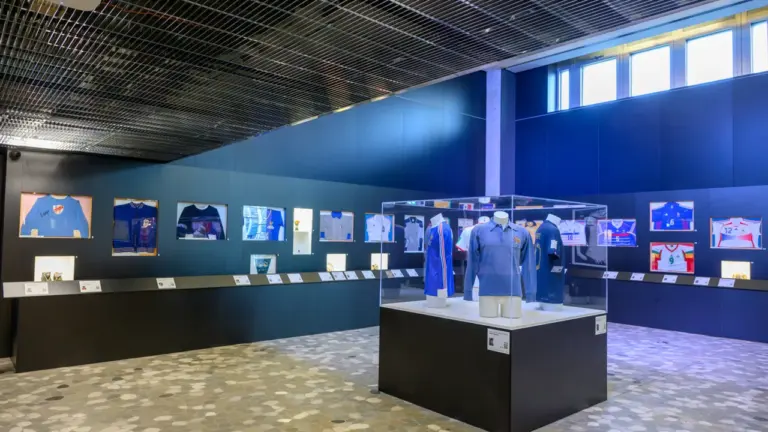 Exposition de maillots de football historiques exposés dans un musée moderne aux murs bleus.