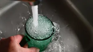 Une main remplit un verre d'eau depuis un robinet de cuisine domestique.