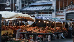 Vue nocturne animée d'un marché traditionnel français avec des étals de fruits frais.