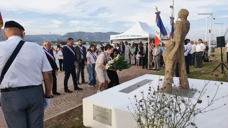 Une cérémonie de commémoration avec des officiels déposant des fleurs devant une statue commémorative.