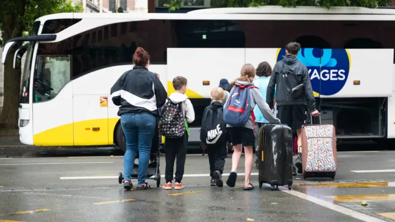 Un groupe de personnes avec des valises se dirige vers un grand autocar blanc.