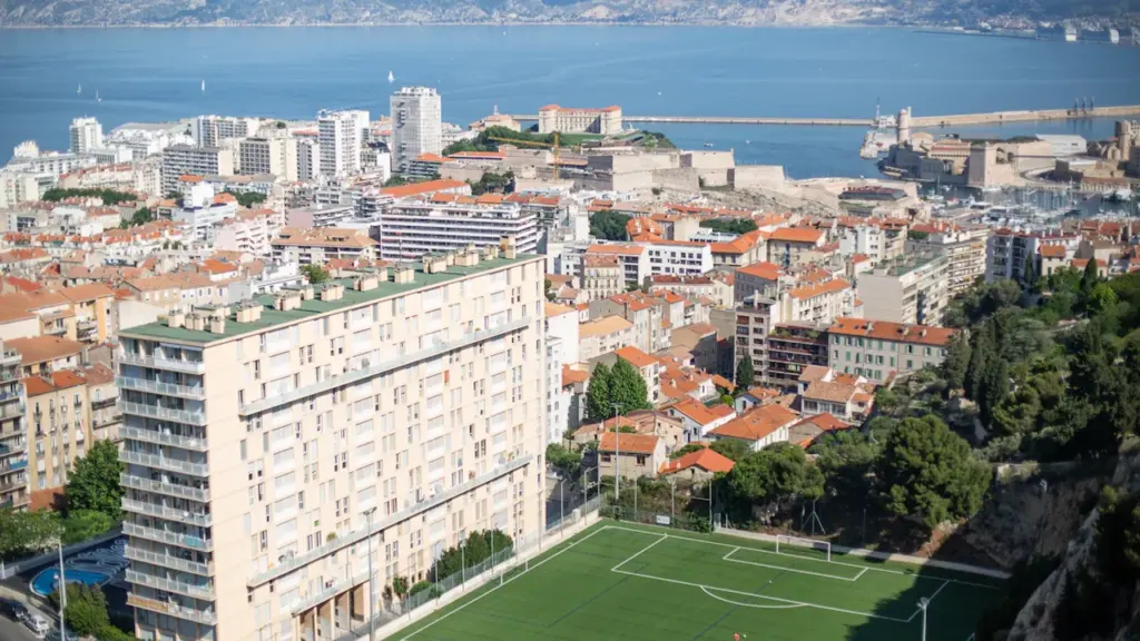 Vue panoramique de Marseille depuis Notre-Dame de la Garde surplombant un terrain de sport.