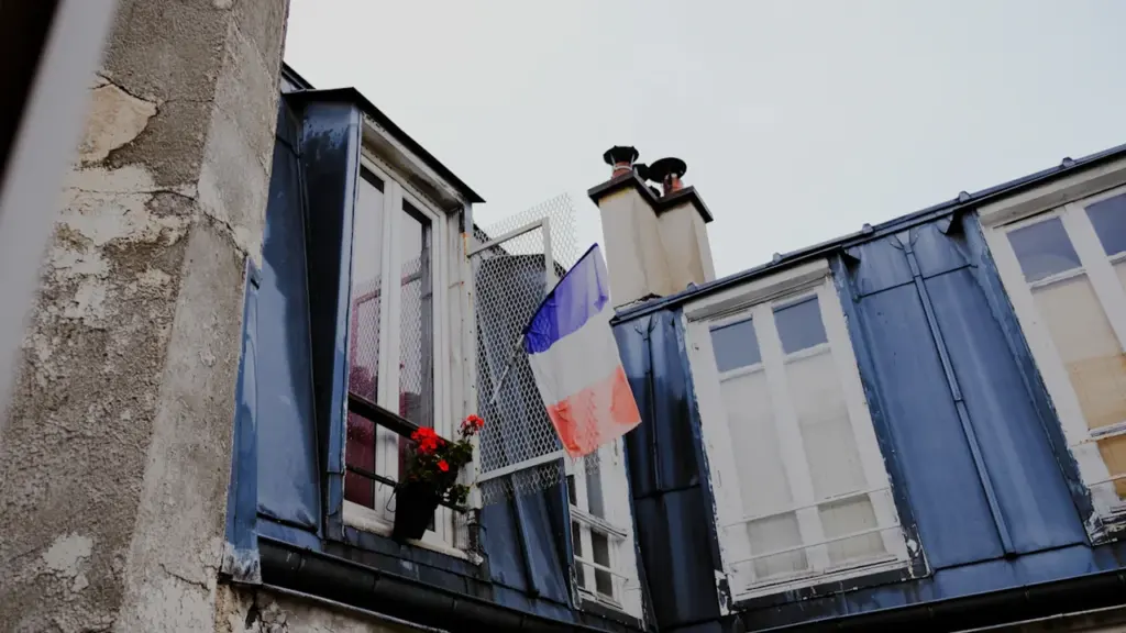 Drapeau français flottant à la fenêtre d'un bâtiment en pierre typique.