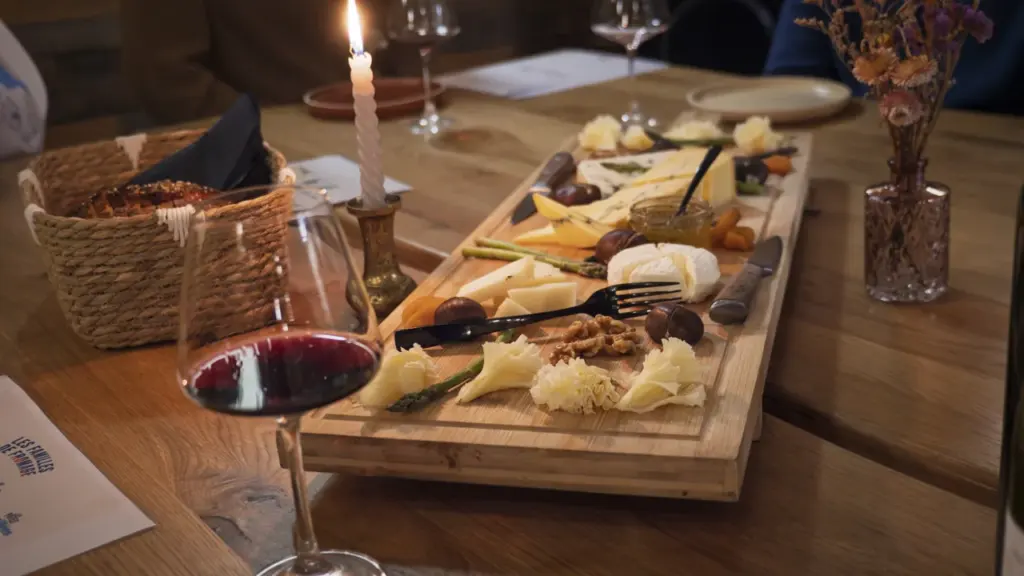 Une planche en bois garnie de divers fromages, noix, fruits et vin rouge.