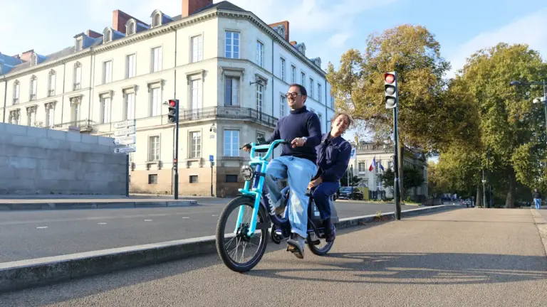 Un couple circulant en vélo tandem dans une rue urbaine ensoleillée à Nantes.