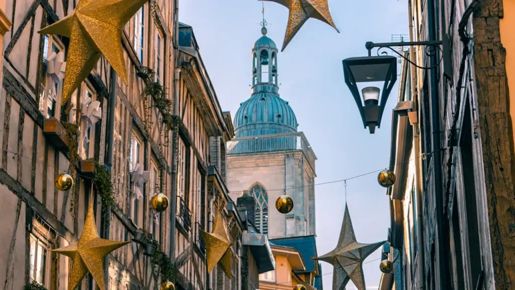 Rue historique de Rouen décorée pour les fêtes avec une tour médiévale en fond.