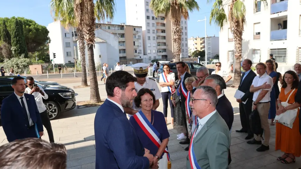 Un groupe de personnes, dont des élus portant des écharpes tricolores, discute en extérieur.
