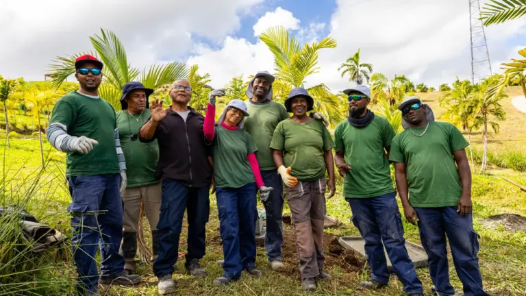 Un groupe de huit travailleurs en uniformes verts sourit dans un champ avec des palmiers.
