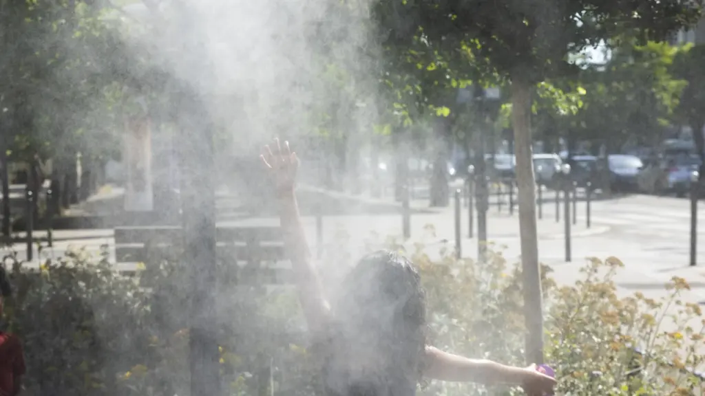 Une personne de dos, bras levés, jouant dans la brume rafraîchissante d'un parc urbain.