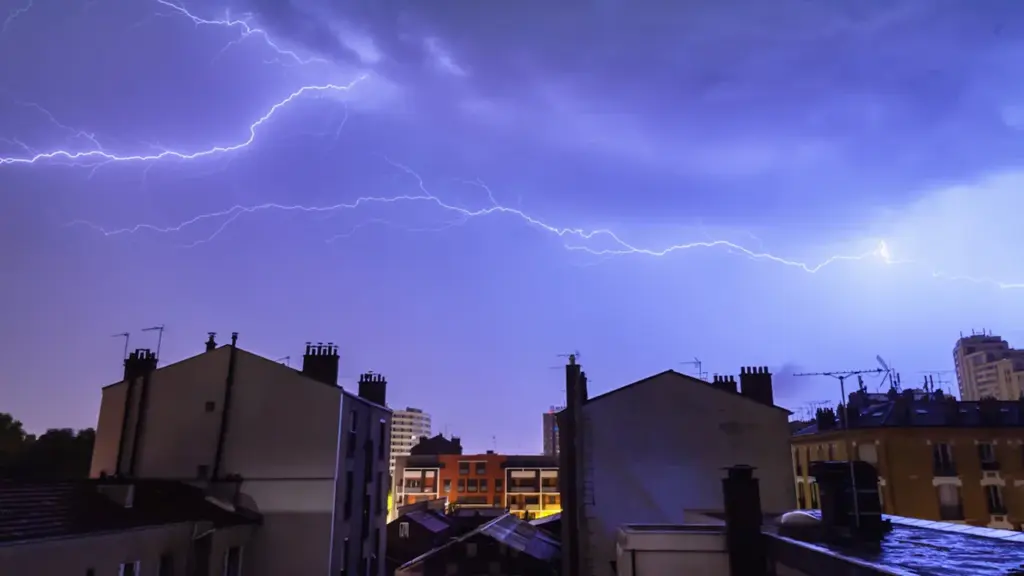 Des éclairs frappent le ciel au-dessus des toits d'immeubles parisiens durant l'orage.