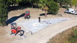 Vue aérienne d'un chantier paysager avec une mini-pelle, un tracteur et des dalles posées.