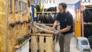 Un mécanicien barbu répare une roue de vélo dans un atelier rempli d'outils suspendus.