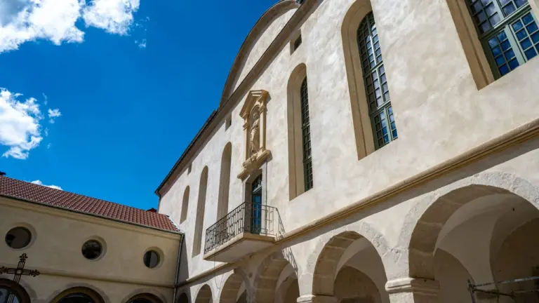 Façade d'un bâtiment historique en pierre avec des arches et un balcon sous ciel bleu.