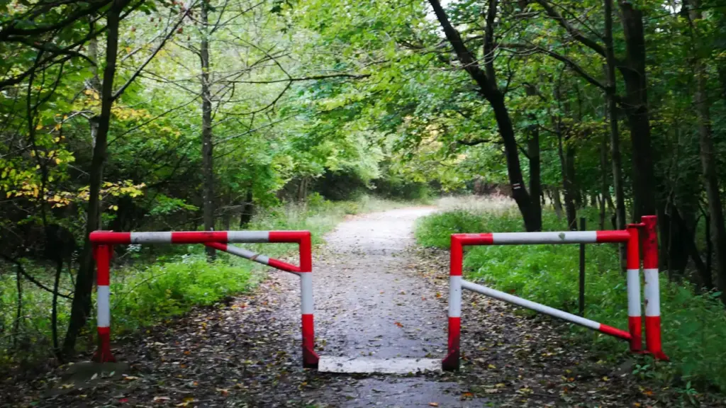 Barrière rouge et blanche bloquant l'accès à un chemin forestier en forêt.