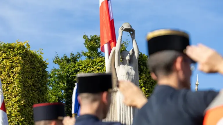 Militaires en uniforme saluant devant une statue de pierre représentant un ange tenant un casque.