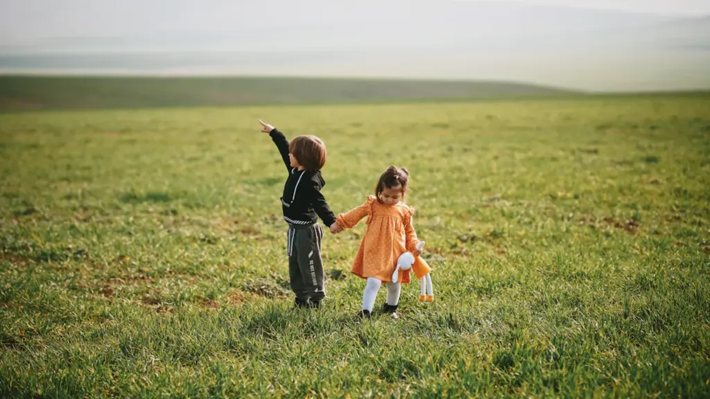 Deux jeunes enfants marchant main dans la main dans un champ verdoyant en France.