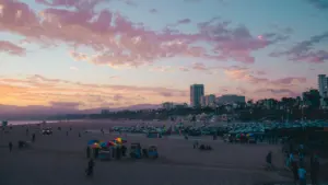 Coucher de soleil vibrant sur une plage fréquentée avec des immeubles en arrière-plan.