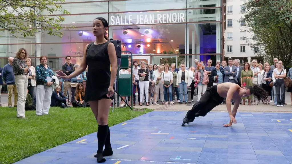 Une femme et un danseur en roller performant devant un public nombreux à l'extérieur.