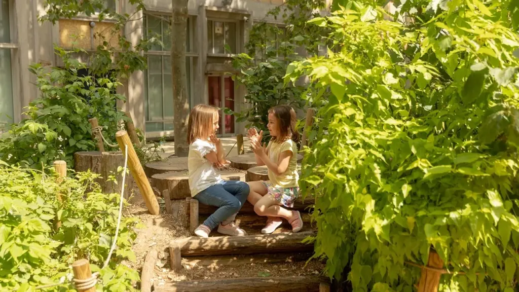 Deux jeunes filles assises sur des rondins de bois, jouant ensemble dans un jardin ensoleillé.