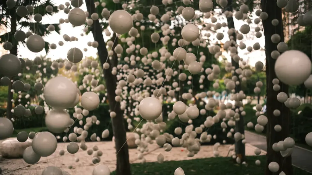 Installation artistique de nombreuses sphères blanches suspendues dans un cadre naturel extérieur.