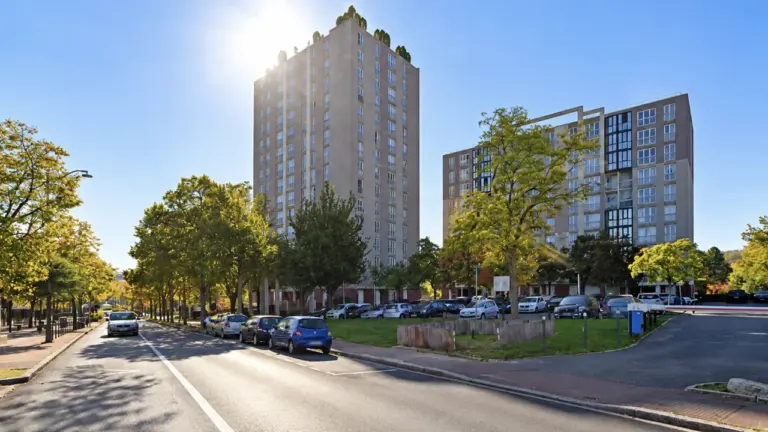 Deux grands immeubles résidentiels modernes bordés d'arbres feuillus sous un ciel bleu ensoleillé.